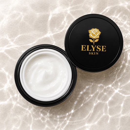 An open black cosmetic jar filled with white cream sits beside a matching black lid printed with a gold rose and the brand name ELYSE SKIN, on a light marble-like surface.