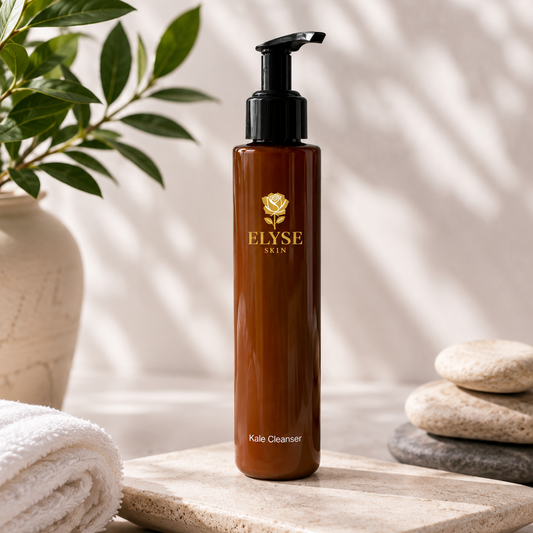 A bottle of ELYSE SKIN Kojic Cleanser standing on a stone tray, surrounded by a rolled towel, a potted plant, and stacked stones in a spa-like setting with soft leaf shadows.