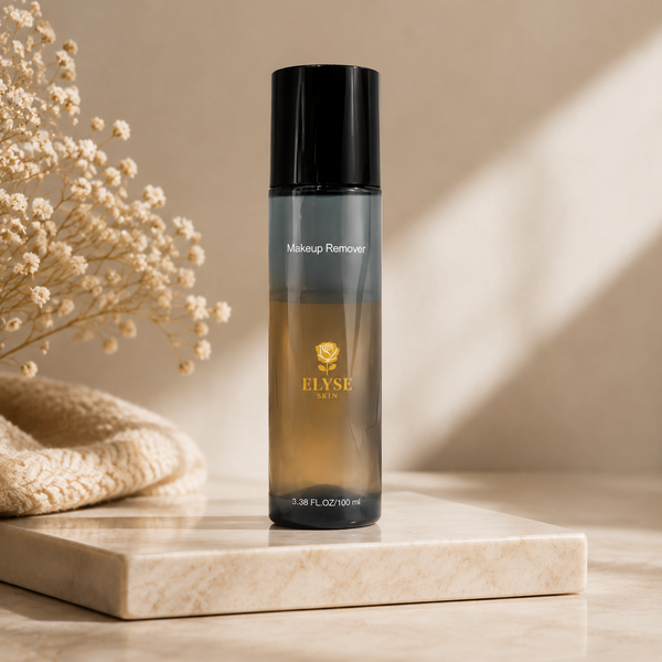 A bottle of ELYSE PARIS Makeup Remover stands on a light marble tray, styled with dried flowers and a beige knit cloth against a warm beige background with soft diagonal shadows.