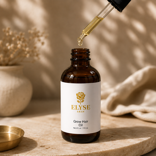 An amber glass bottle of ELYSE SKIN Grow Hair Oil with a white label and gold logo, shown on a stone surface with a glass dropper dispensing golden oil above it. The background features warm beige tones, soft shadows, and dried floral decor.