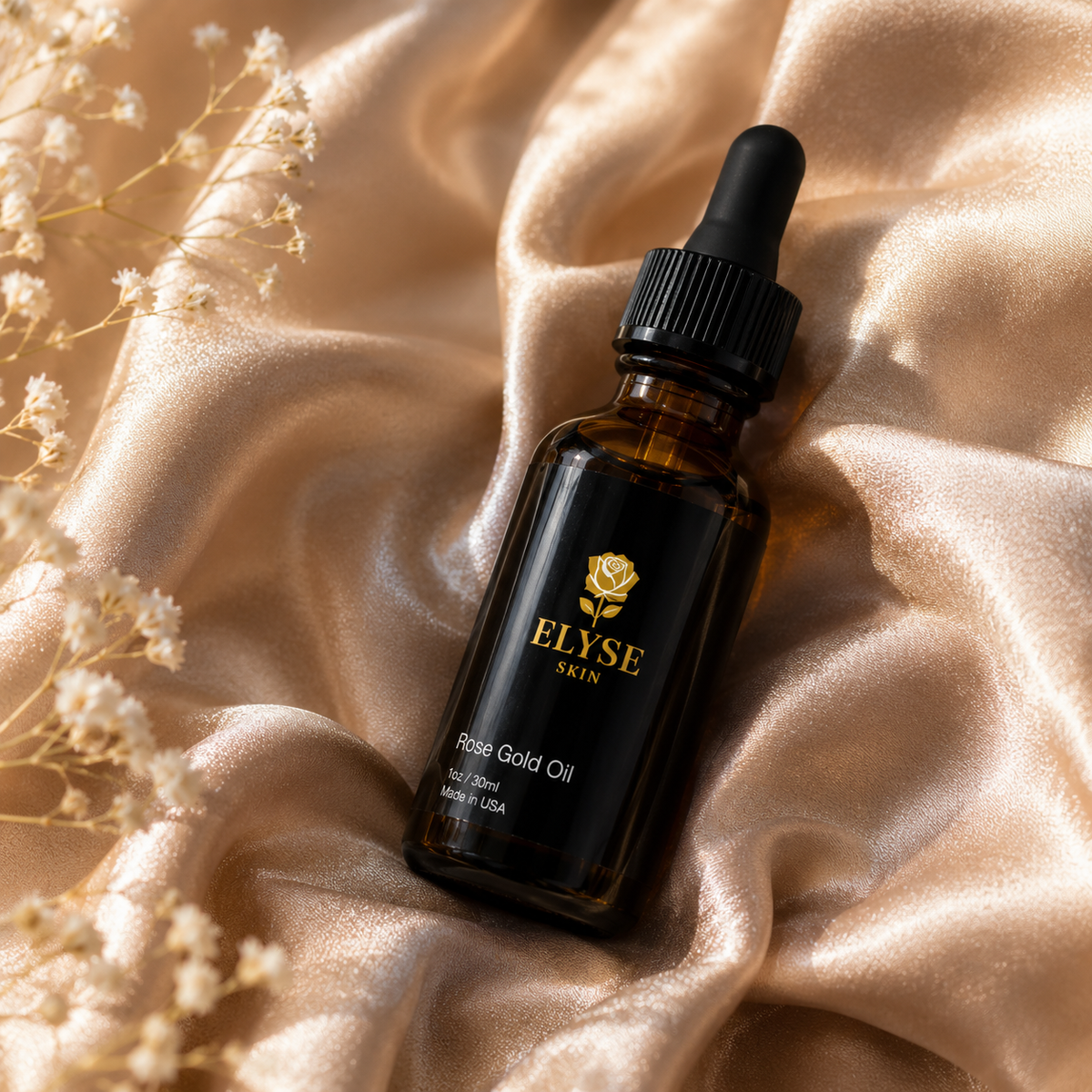 A bottle of ELYSE SKIN Rose Gold Oil with a black dropper cap, resting on draped champagne-colored satin fabric with small white flowers in the corner.