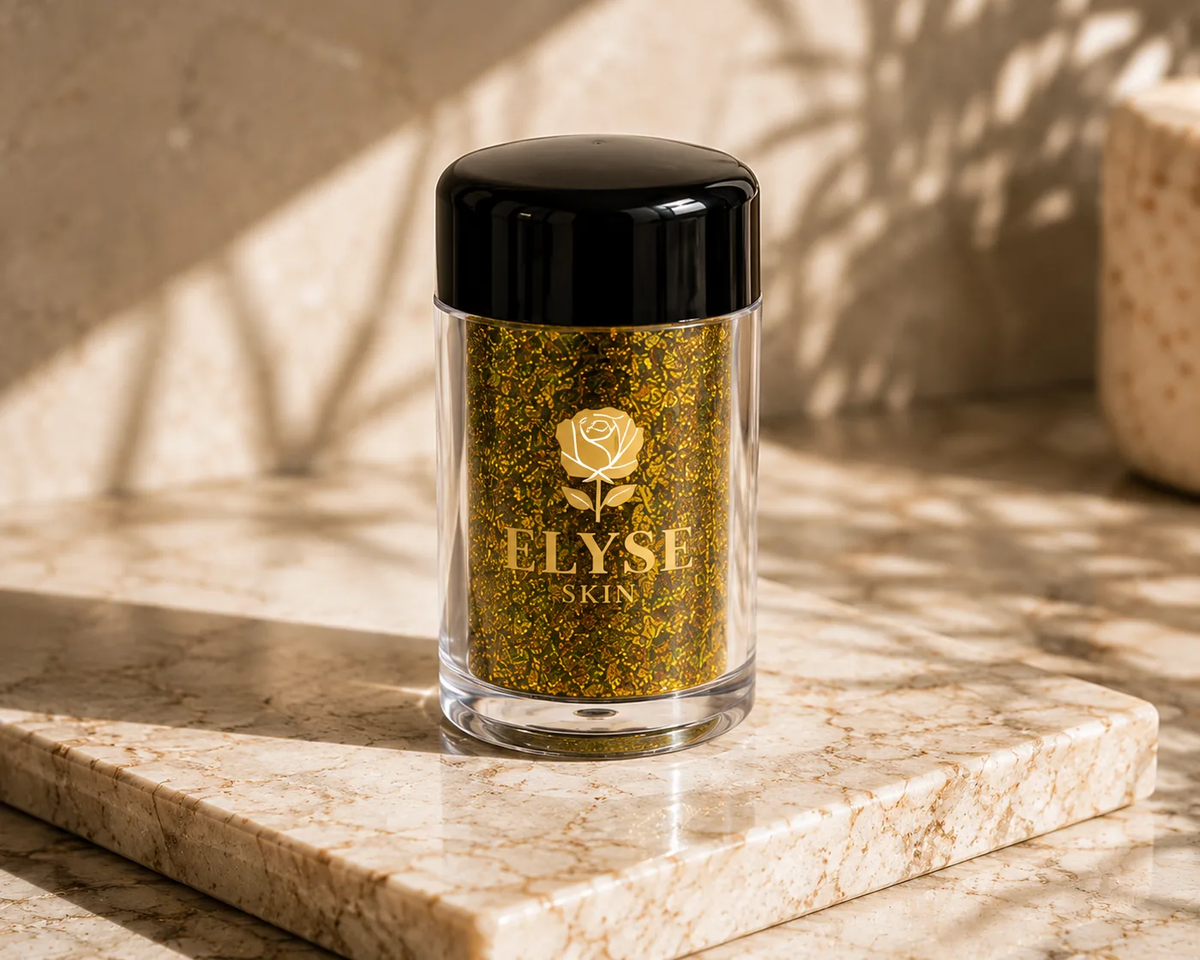 A clear jar of gold glitter makeup with a black lid, featuring the brand name 'ELYSE SKIN' printed in gold on the front, set on a marble slab with warm natural shadows.