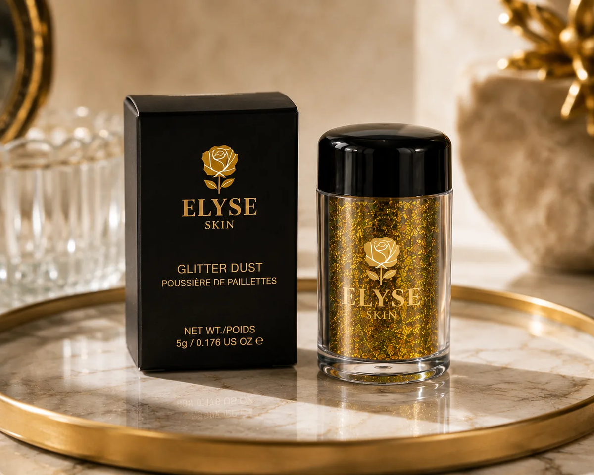 A jar of ELYSE SKIN glitter dust next to its black packaging box, both featuring a gold rose logo, displayed on a marble tray with a gold rim.